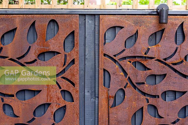 Contemporary garden in Wandsworth. Decorative rusty metal panels on wood fence.