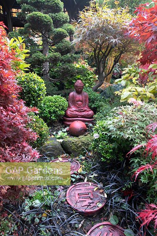 Red buddha statue set amongst autumnal colours and stepping stones at Four Seasons garden, Walsall, West Midlands, in October