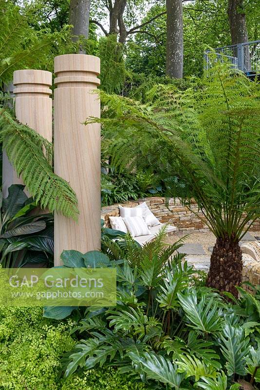 Dicksonia Antarctica Tree fern stands over circular stone sunken seating area surrounded by stone columns. The Time In Between by Husqvarna and Gardena - RHS Chelsea Flower Show 2015. Sponsor: Husqvarna and Gardena.