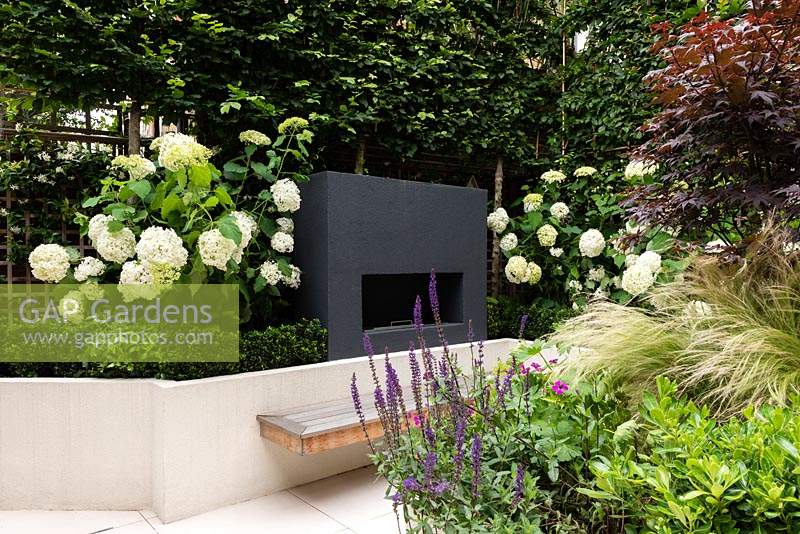 An outdoor fireplace on raised bed alongside Hydrangea arborescens 'Annabelle' with floating bench seating below