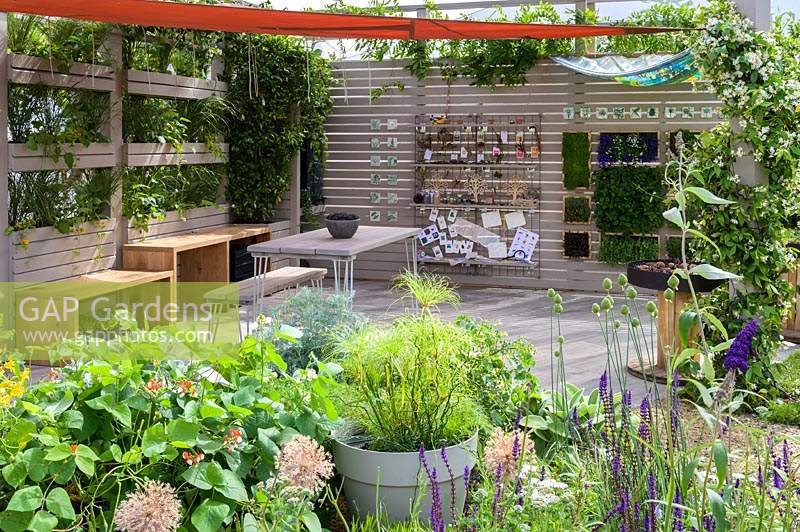Outdoor room with removeable canvas canopy roof, plant screen, table and chairs and planting of herbs and vegetables, with Nasturtiums and climbing french beans - The Year of Green Action Garden - RHS Hampton Court Palace Garden Festival 2019. Sponsors: Defra.