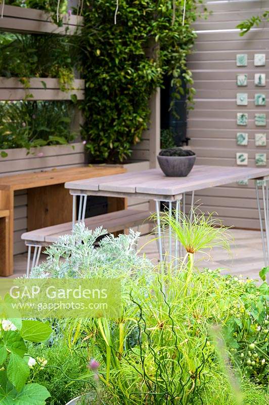 Outdoor room with table and chairs and planting of herbs and vegetables - The Year of Green Action Garden - RHS Hampton Court Palace Garden Festival 2019. Sponsors: Defra.