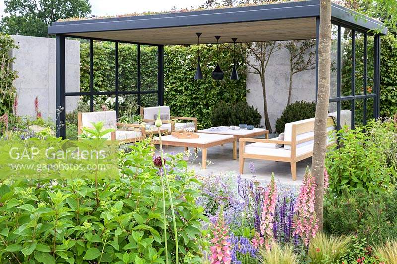Timber table and chairs on slab patio -The Viking Cruises Lagom Garden - RHS Hampton Court  Palace Garden Festival 2019  - Designer: Will Williams