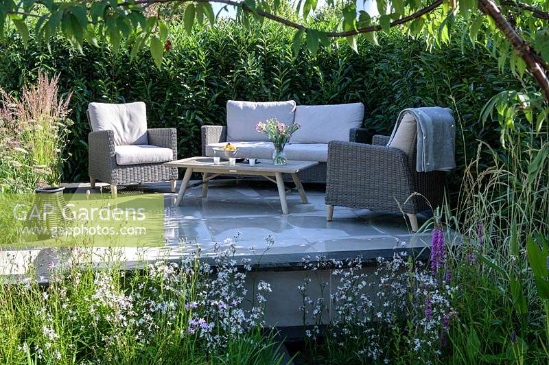 Raised patio with outdoor sofa and armchairs - APL - A Place To Meet Garden - Hampton Court Palace Garden Festival 2019.