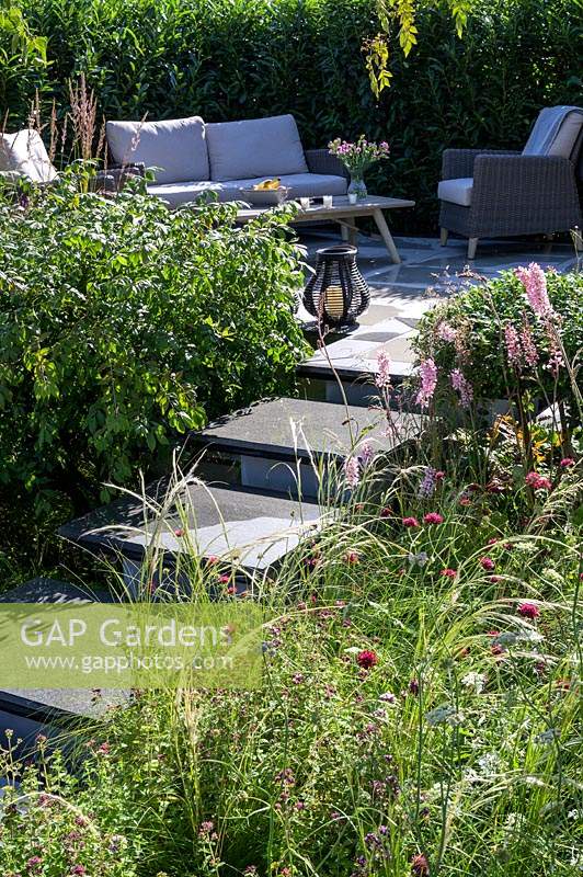Stone steps leading to raised patio with outdoor sofa and armchairs - APL - A Place To Meet Garden - Hampton Court Palace Garden Festival 2019.