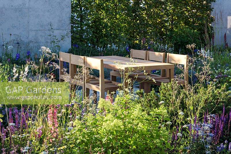 Timber table and chairs on slab patio - The Viking Cruises Lagom Garden - RHS Hampton Court  Palace Garden Festival 2019.