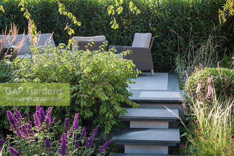 Stone steps leading to raised patio with outdoor sofa and armchairs -APL - A Place To Meet Garden - Hampton Court Palace Garden Festival 2019  
Designer: Cherry Carmen