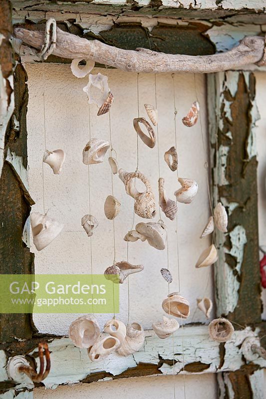Detail of recycled piece of timber furniture with peeling paint mounted on a wall decorated with handmade shell mobile.