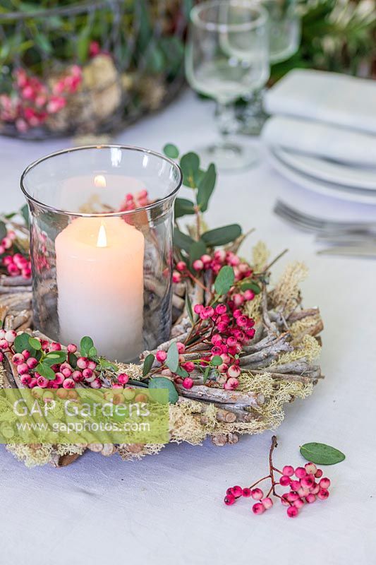 Pillar candle in storm lantern surrounded by wooden wreath with moss, rowan berries and Eucalyptus