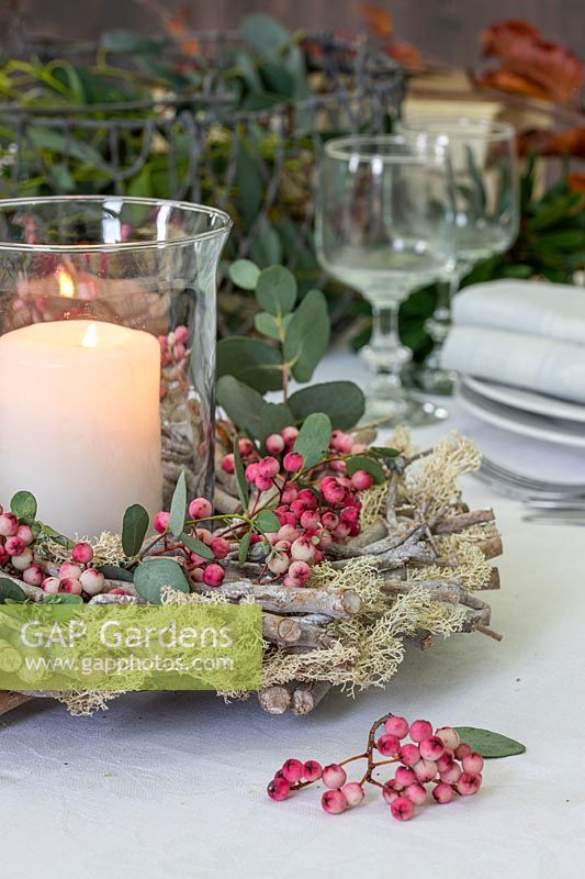 Table decoration, comprising: pillar candle in storm lantern surrounded by wooden wreath with moss, sorbus - Rowan - berries and Eucalyptus foliage