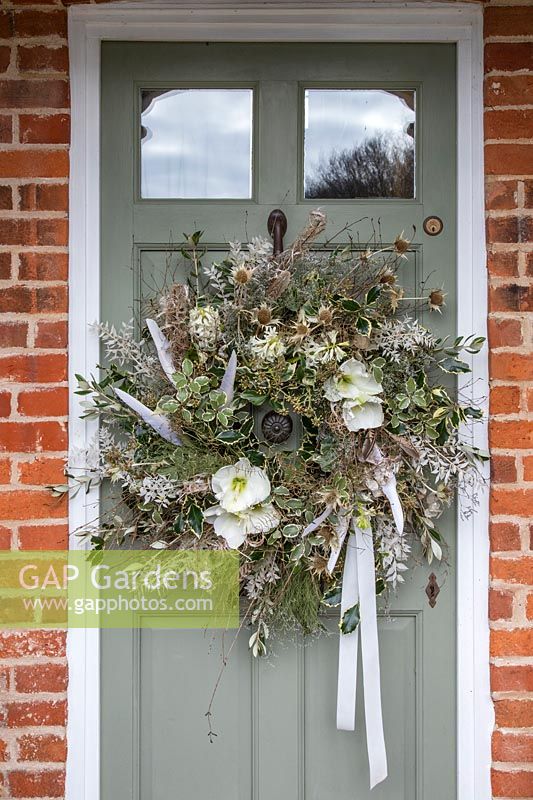 Finished white themed wreath with feathers hanging on sage green door of cottage