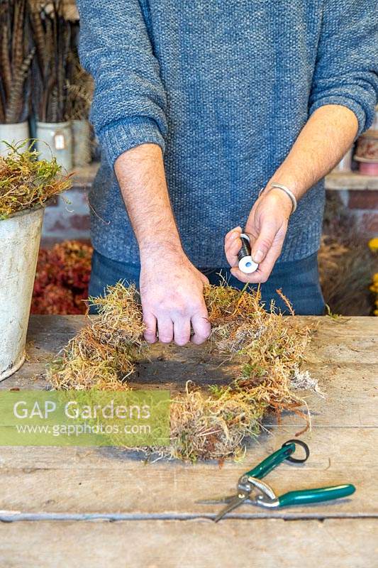 Man wiring moss to wire frame to from base of wreath