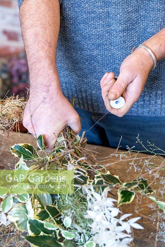 Man wiring bundle of mixed foliage on to wreath