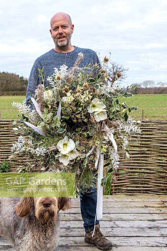 Man holding finished white themed wreath with feathers 