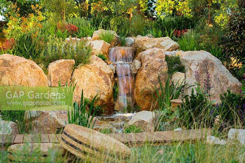 A naturalistic looking waterfall made from rustic sandstone rocks and planted with a variety of shrubs and grasses 