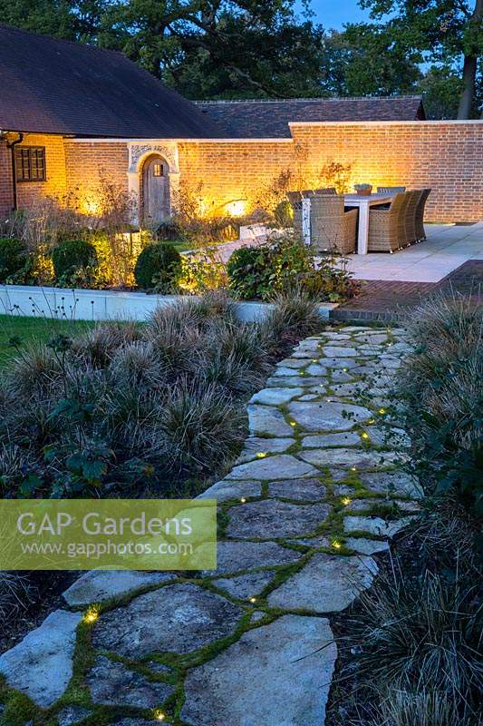 View up crazy paving path with embedded floor lighting to outside eating area in large Surrey Garden 