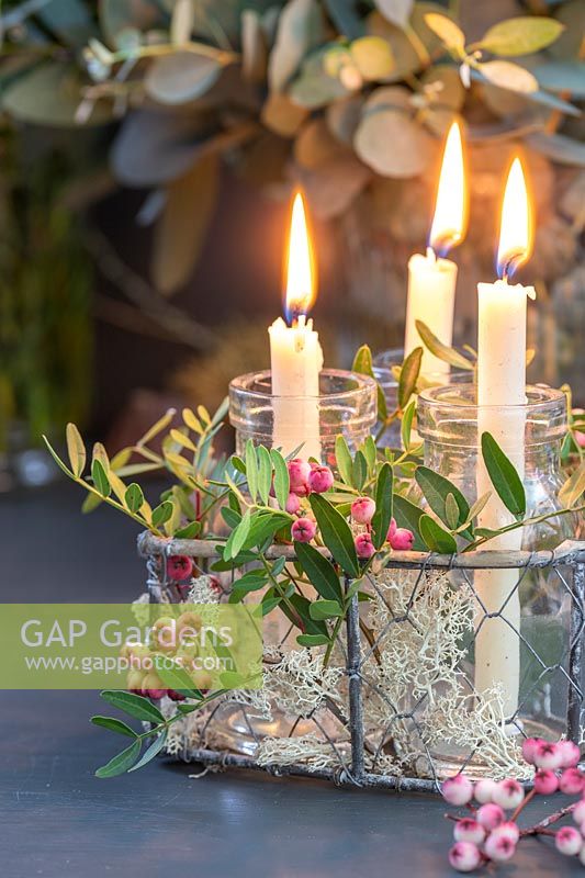 Arrangement with candles in jam jars, metal wire frame and pink rowan berries and foliage