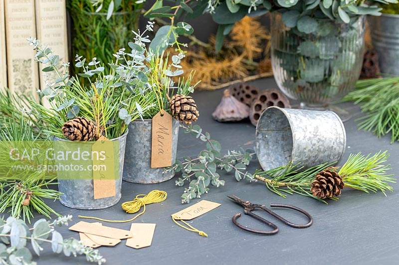 Name tags hung from metal pots filled with mixed green foliage and pine cones