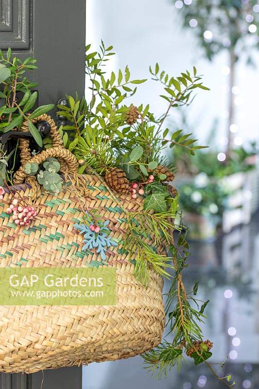 Woman basket with a mix of foliage hanging in hallway ready for use at Christmas