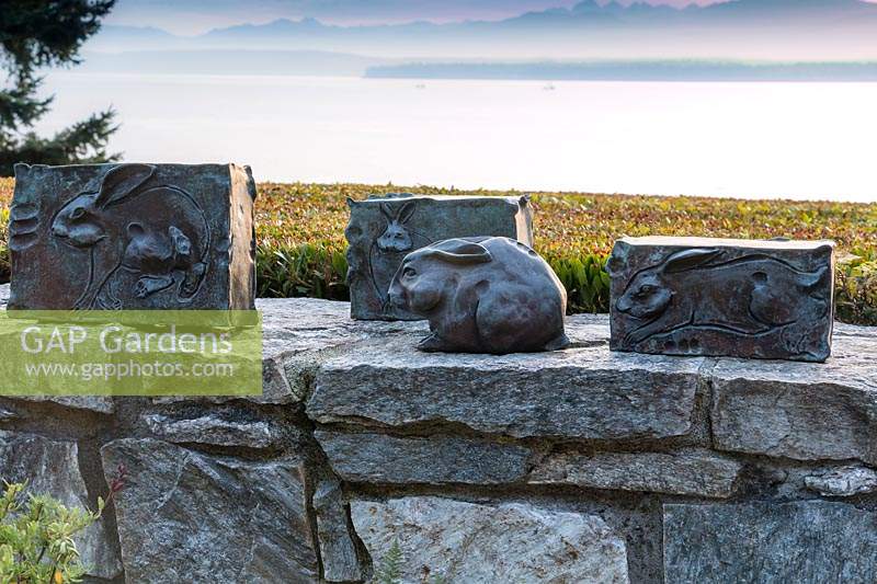 The low stone wall, framed by a sheared hedge of Morella californica doubles as an art gallery for this series of bronze rabbit sculptures.