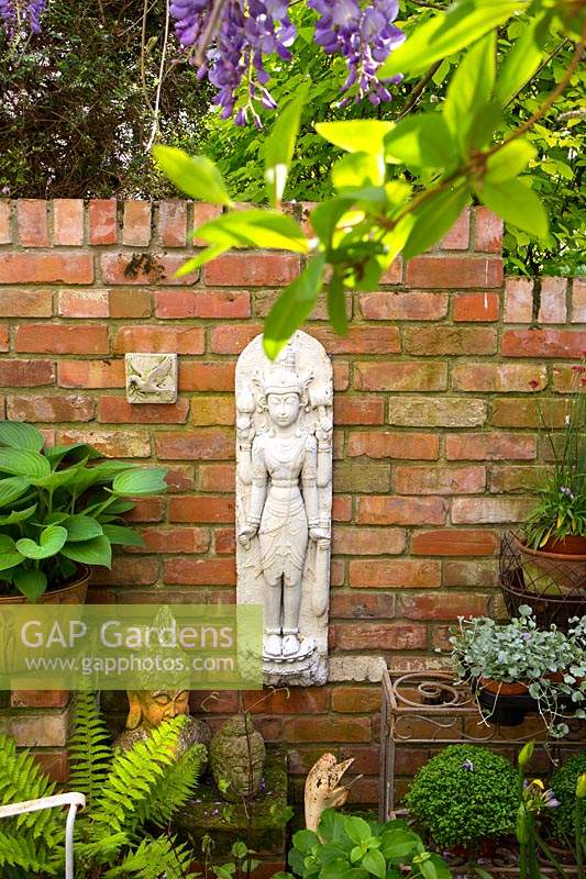 Brick wall with wall plaques and Buddha heads, all displayed alongside containers with Hosta and other perennials 