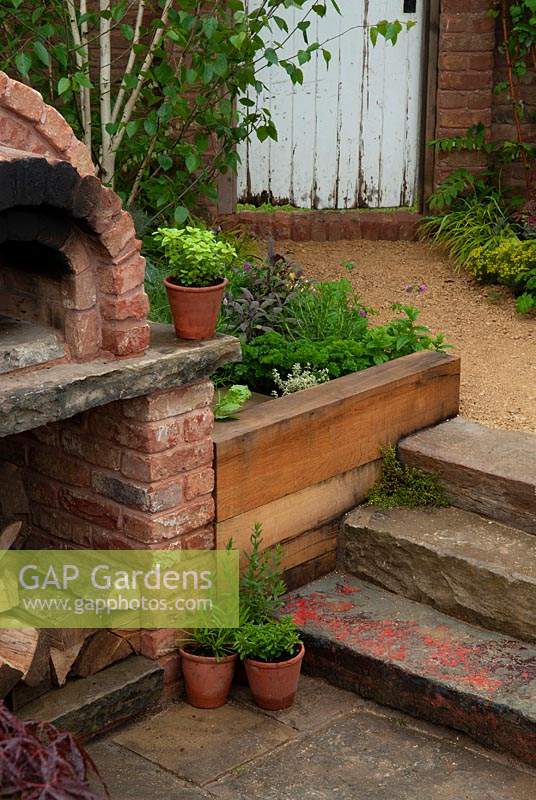 Outdoor brick oven set into raised herb border with stone steps leading down to it - RHS Malvern Spring Festival