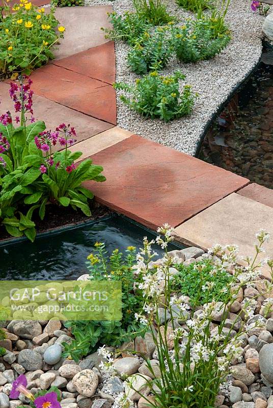 Path of mixed paving slabs over running stream with alpine plants in gravel and stones - RHS Chelsea Flower Show