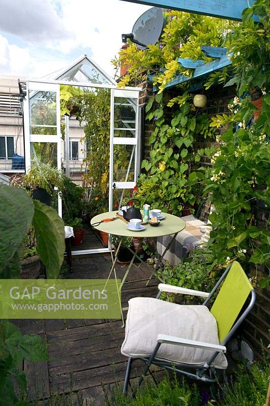 A small greenhouse on a London roof terrace. A small table and deck chair