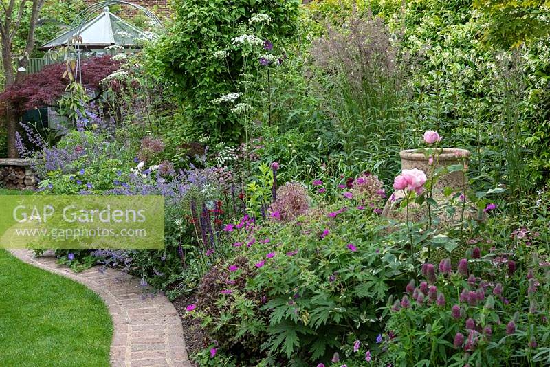 A brick edging separates the lawn from an herbaceous border of catmint, roses, ammi, stipas, hardy geraniums and alliums, leading to a work area in furthest corner of irregularly shaped plot.