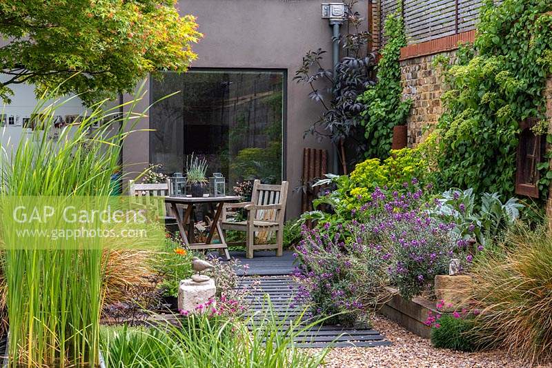 A path is made from wood off-cuts fixed at equal intervals beneath the gravel. Seating area is outside the studio,raised bed with black elder, euphorbia, cardoon and Erysimum 'Bowles Mauve'. Climbing hydrangea