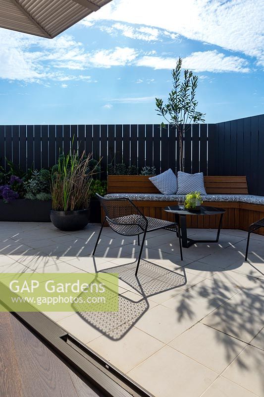 Contemporary outdoor setting in front of bespoke banquette bench seating with a group of potted plants and a raised garden bed.