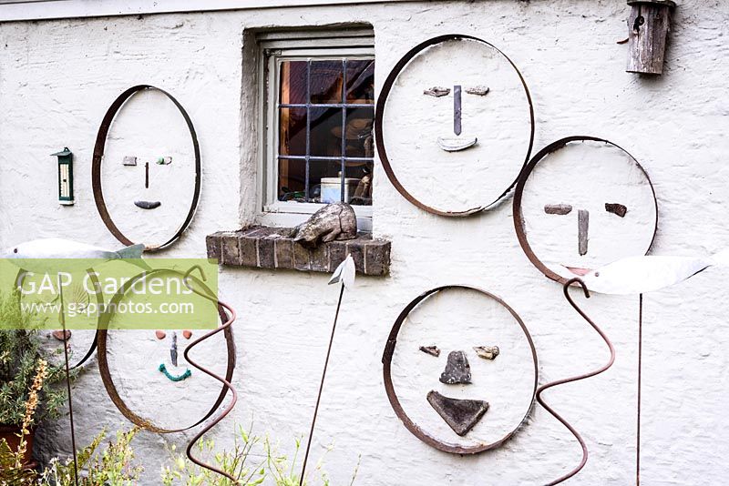 House wall decorated with faces made using the empty frames of vintage sieves with various pieces of wood, shells and other material as features