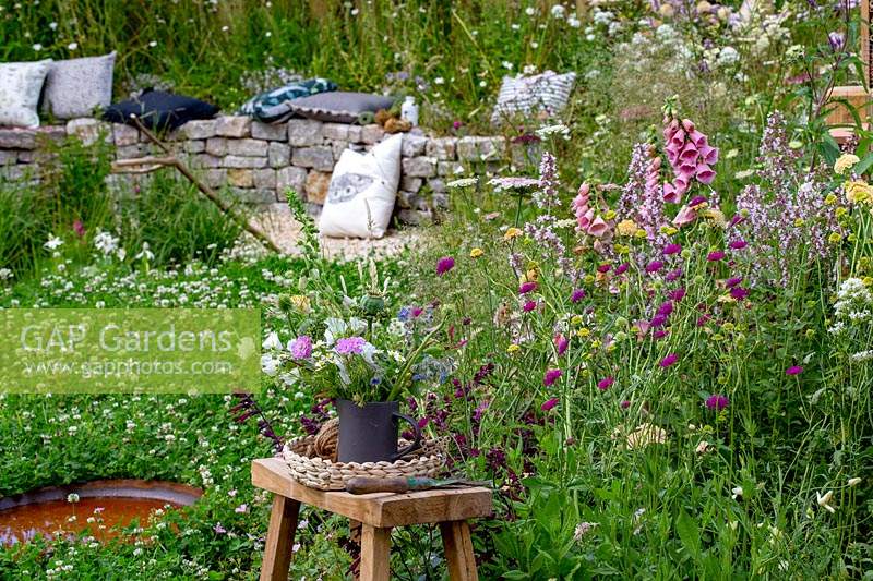 Springwatch Garden - Hampton Court Flower Show 2019 - designer, Jo Thompson - stool with a vase display of cut flowers in wildlife friendly garden