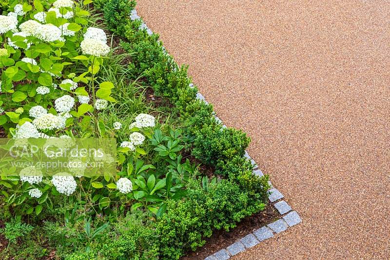 View from above of angular borders edged with cobbled granite and planted with woodland plants such as Hydrangea and Buxus