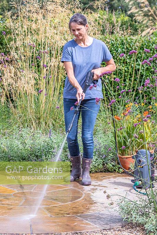 Woman using pressure washer to clean circular patio. 