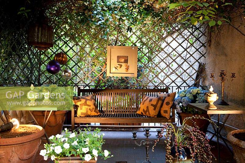Garden bench and potted plants are sheltered by trellis and climbing plants. 

