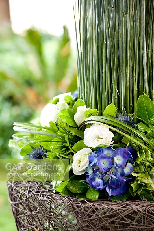 Close up of basket filled with ears of corn, Lisianthus, Hydrangea, Eryngium, Beargrass and variegated Ivy.