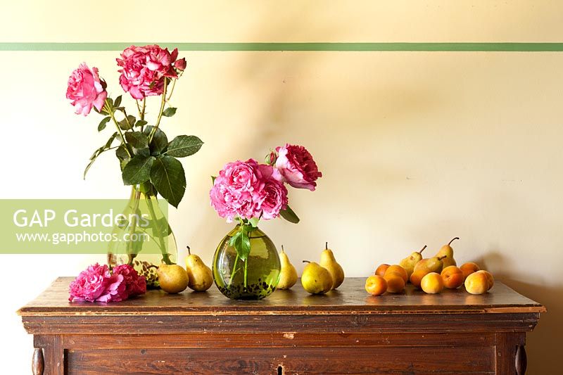 Vases of roses and mixed fruits displayed on a cabinet