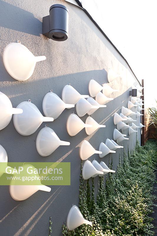 Garden wall decorated with white plastic funnels with ficus pumilia at the bottom of the wall