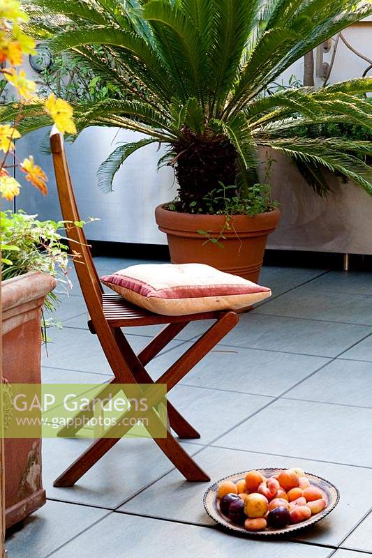 Folding wooden chair with cushion on paved terrace 