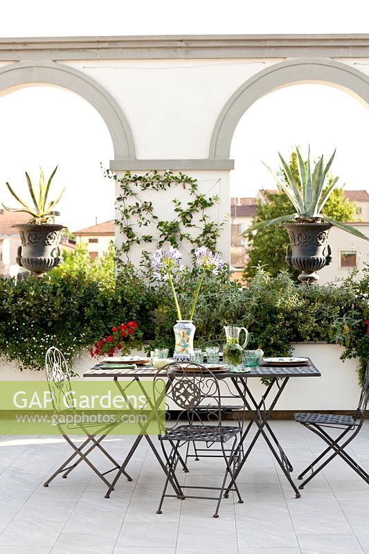 Dining area on classic roof terraces with large planters and urns in archways with view to town beyond