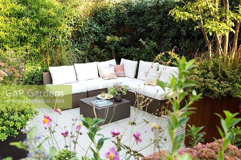 Corner sofa seating area in terrace garden, surrounded by plants in raised beds.