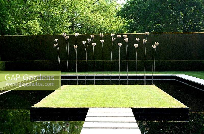 Contemporary water feature -  pool with floating stepping stone path to central grass area and metal sculptures