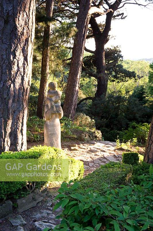 Sculpture of woman and child beside stone path beneath Pinus trees 
