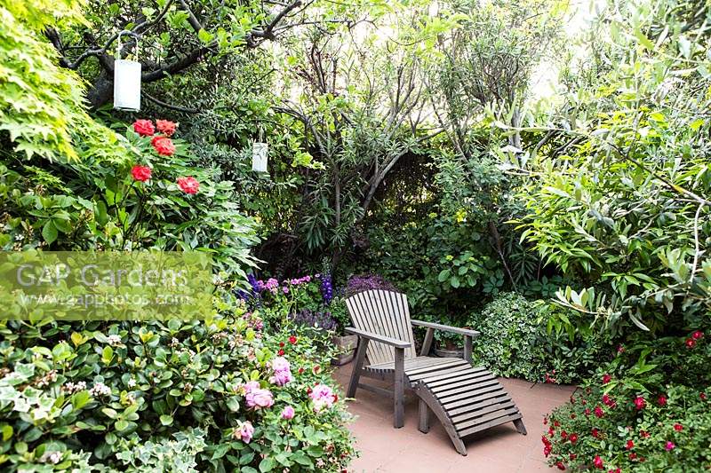 Enclosed relaxing patio area with recliner surrounded by mixed planting.

