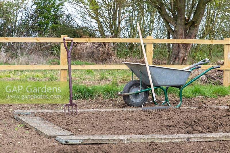 Wheelbarrow, fork, rake and wooden boards, tools and equipment for making a new kitchen garden