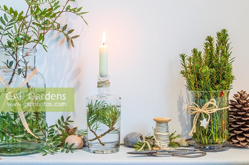 Wooden shelf decorated with a candle in a bottle and freshly cut green foliage