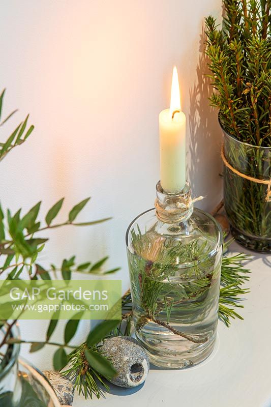 Wooden shelf deocrated with a candle in a bottle and freshly-cut green foliage