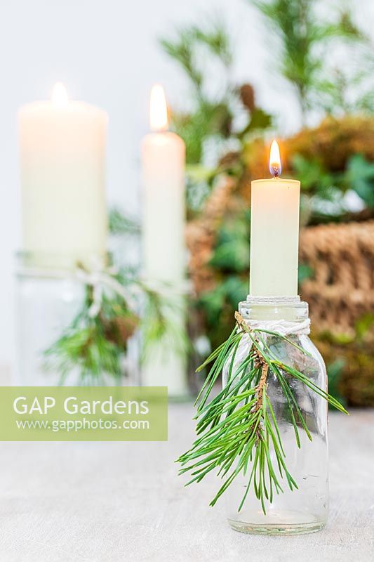 Candles in small glass bottles adorned with cut pine foliage