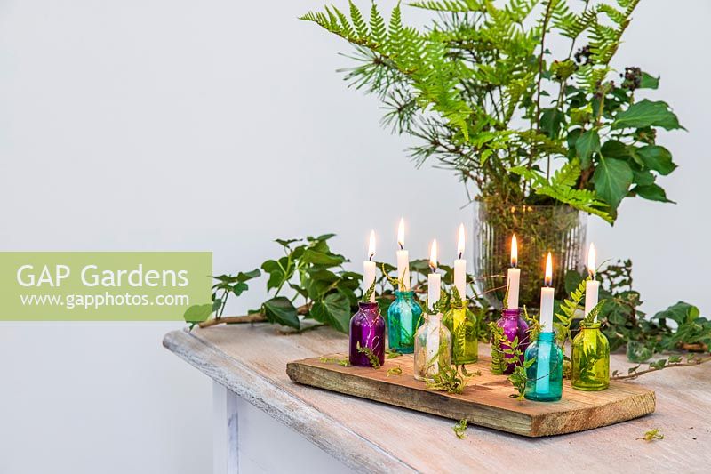 Colourful miniature glass bottles used as candle holders decorated with Fern, Ivy and moss